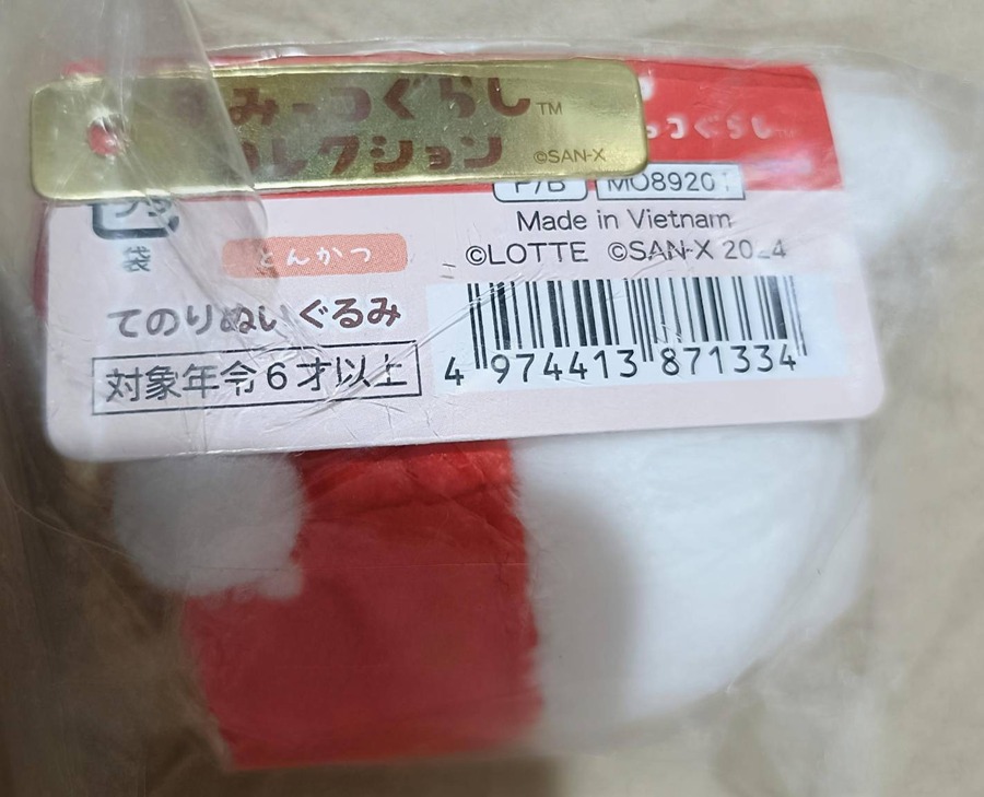 ロッテ×すみっコぐらし てのりぬいぐるみ「とんかつ」のタグ。品番MO8920x、©LOTTE ©SAN-X 2024、Made in Vietnam、対象年齢6才以上の表記が確認できる。