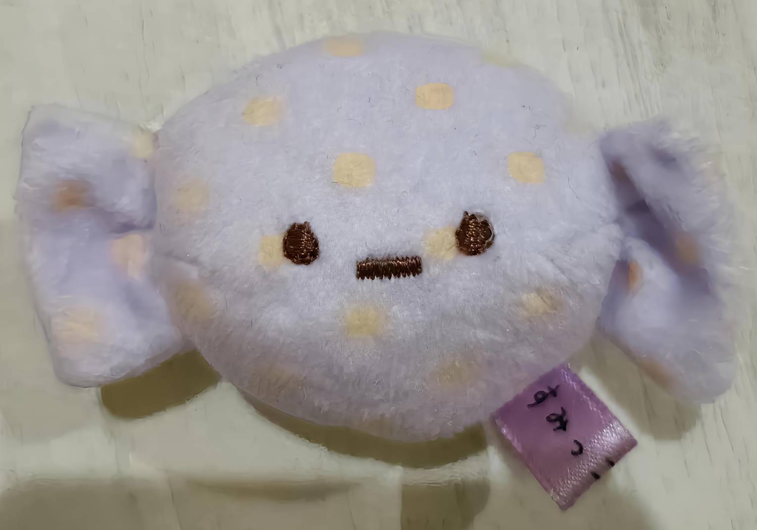 おばけキャンディのマスコット単体。薄紫ポルカドット生地・ブラウン刺繍の顔・両サイドのキャンディねじり飾り・紫の小タグ付き