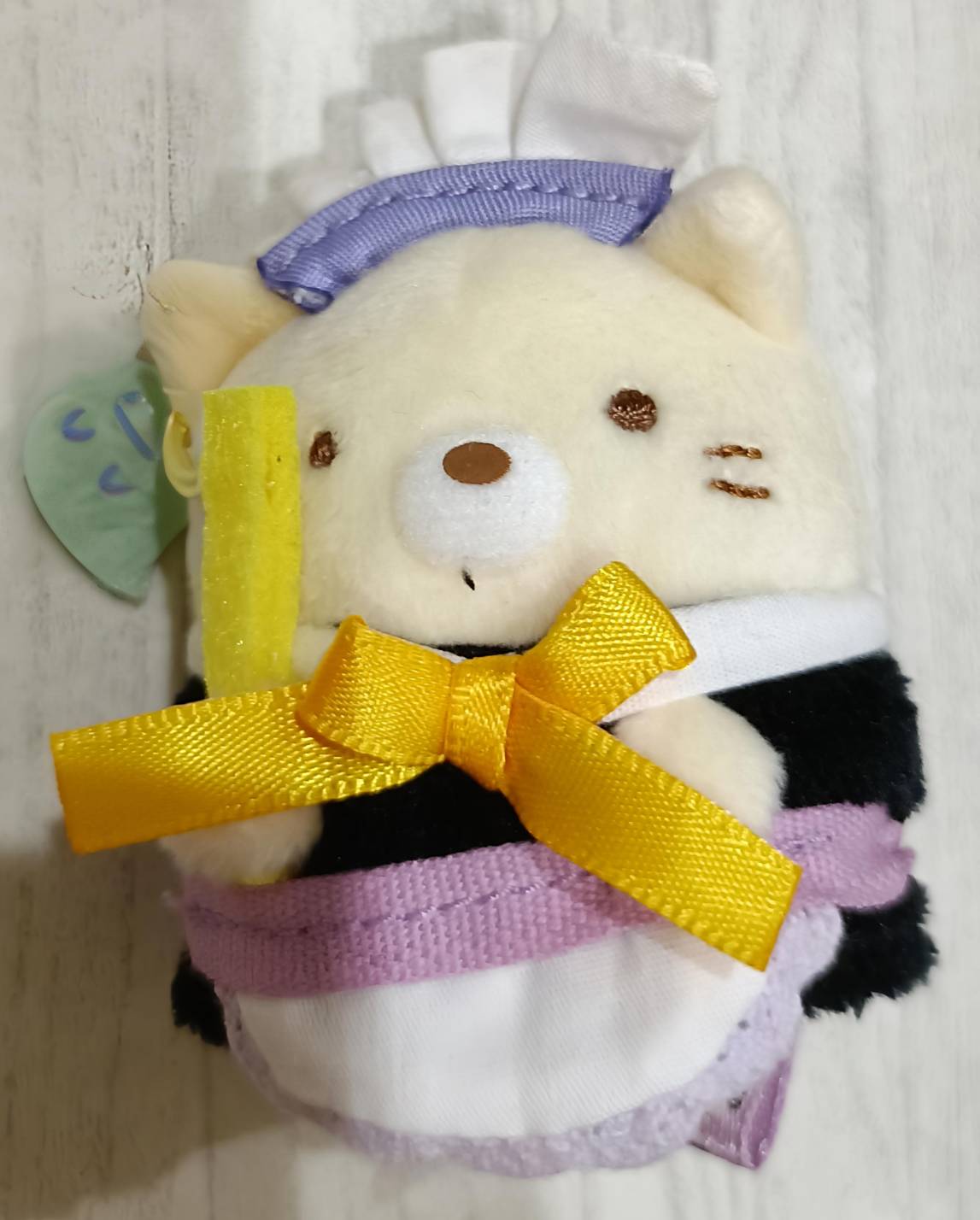 ねこのマスコット単体正面。白黒ボーダードラキュラ衣装・黄色大リボン・紫ハーフムーン飾り・緑丸タグ付き