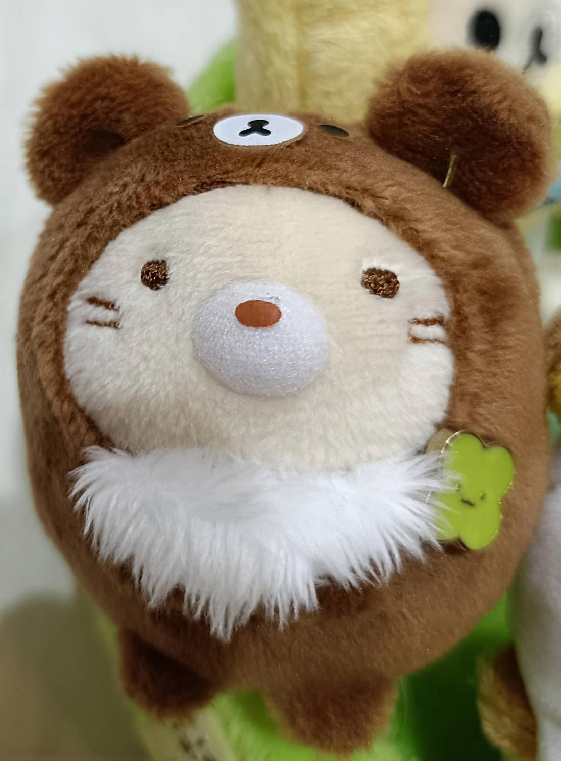 ねこがリラックマの着ぐるみを着たマスコット。ふわふわの白いひげと大きな白い鼻が特徴、緑のクローバーチャームあり