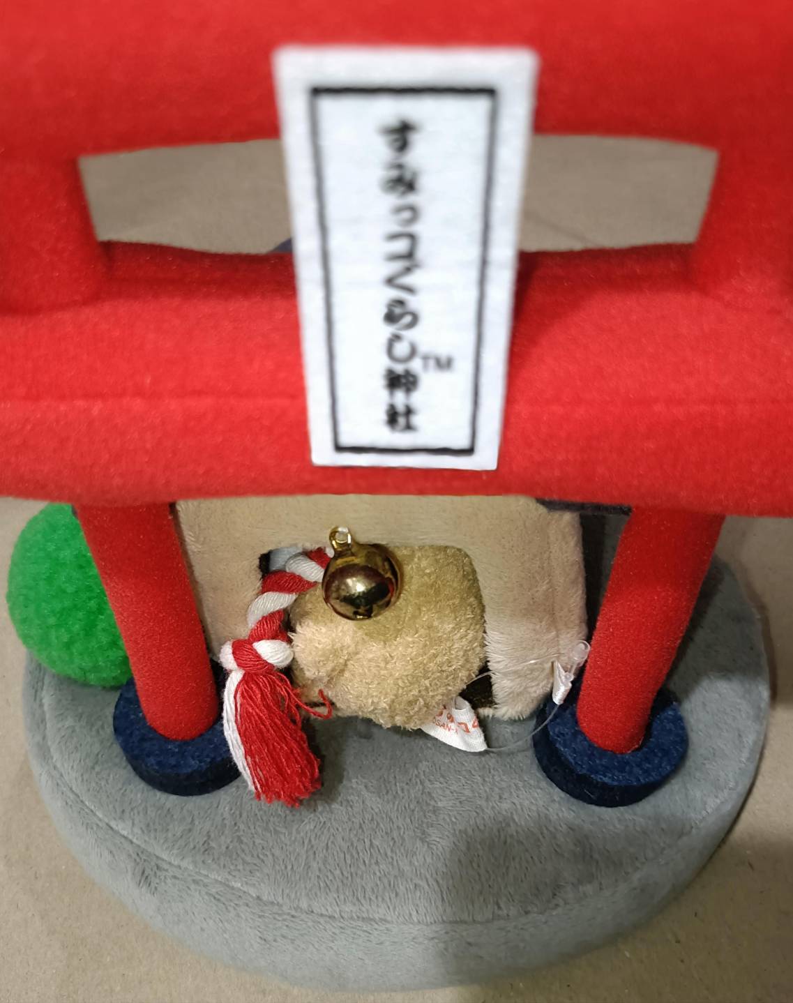 鳥居と看板「すみっコぐらし神社™」のクローズアップ。お社入口のしめ縄(紅白)と金の鈴が見える。