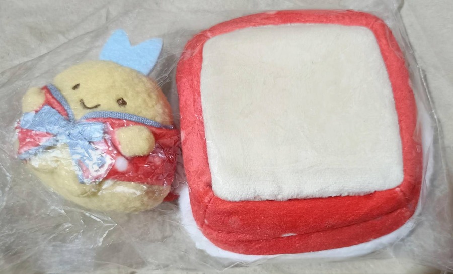とんかつ（黄色）のてのりぬいぐるみと、赤×白のカツクッション型ぬいぐるみのセット。青いリボンの赤い衣装が特徴。