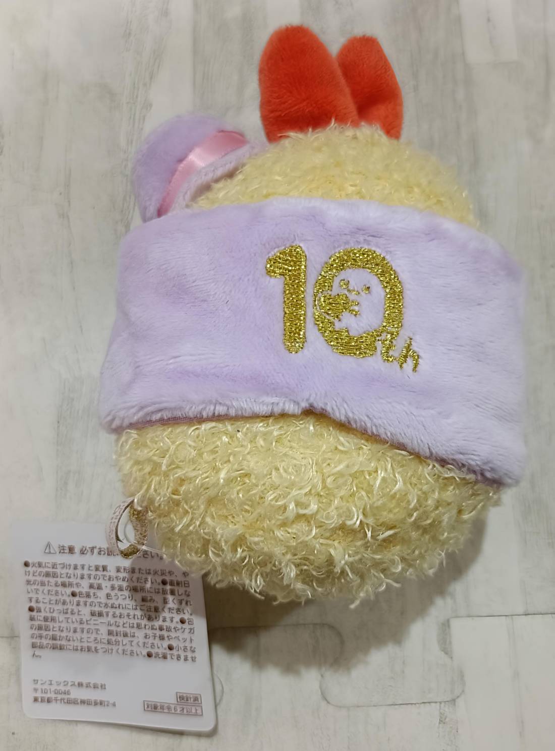 ぬいぐるみ背面。ラベンダー色の帽子に金刺繍で「10th」の文字と10周年すみっコマークが入っている。
